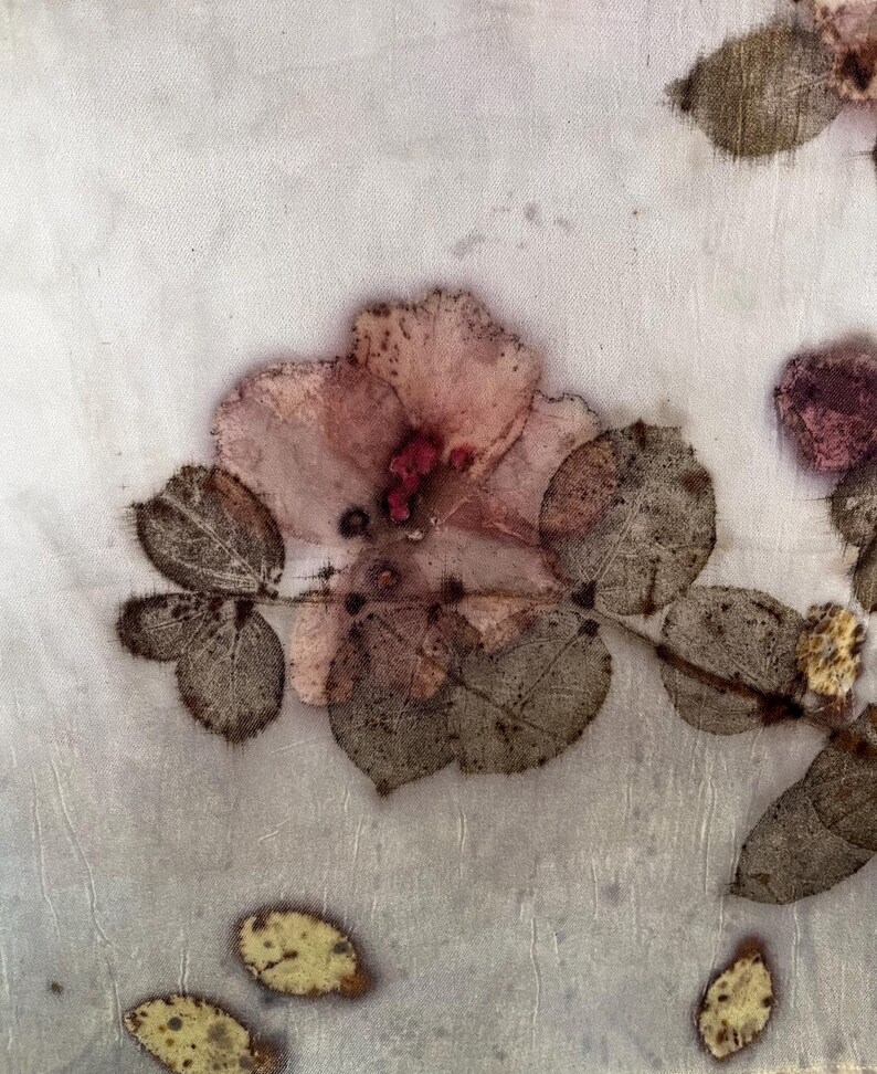 May include: A light-coloured fabric featuring botanical prints of a pink flower and dark brown leaves. The textile displays organic, pressed-plant patterns with visible veins and textures, creating a natural, earthy aesthetic across the surface.