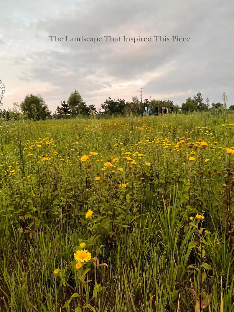 May include: A field of tall green grass and numerous yellow wildflowers under a cloudy sky. The text "The Landscape That Inspired This Piece" is centered at the top of the image. The horizon features a line of dark green trees and distant figures.