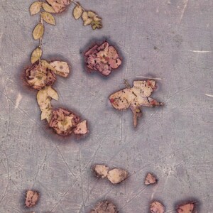 May include: A textured, muted purple surface decorated with botanical imprints of pressed flowers and leaves. The design features scattered floral shapes and a leafy vine pattern in faded brown and tan tones, creating a natural, organic appearance.