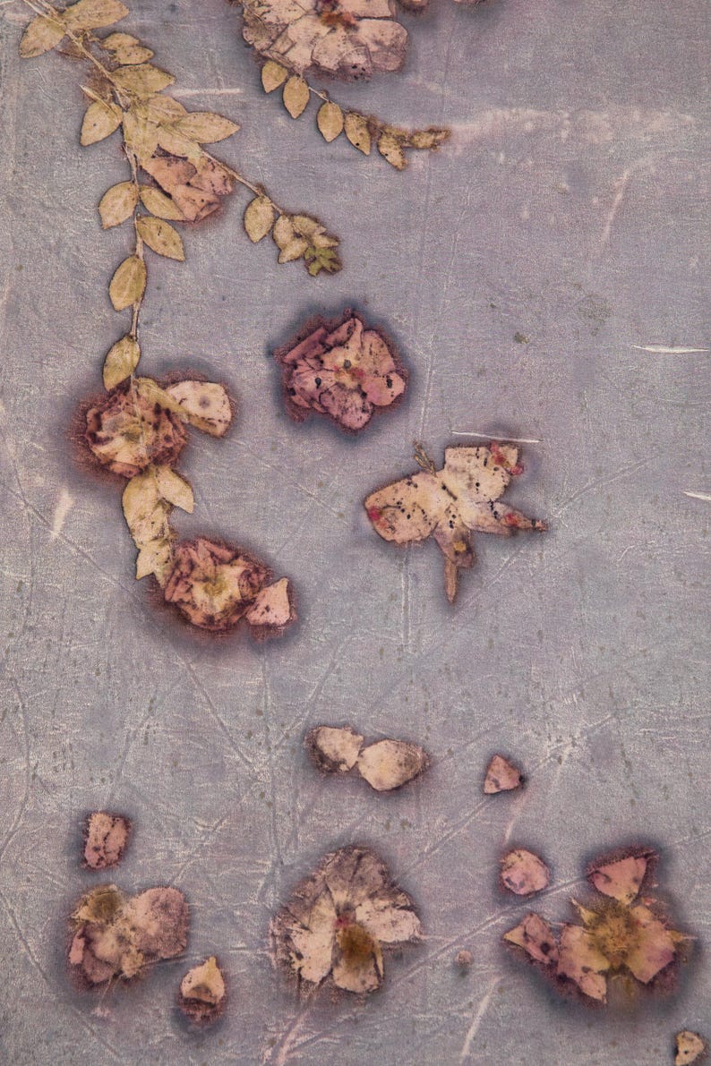 May include: A textured, muted purple surface decorated with botanical imprints of pressed flowers and leaves. The design features scattered floral shapes and a leafy vine pattern in faded brown and tan tones, creating a natural, organic appearance.
