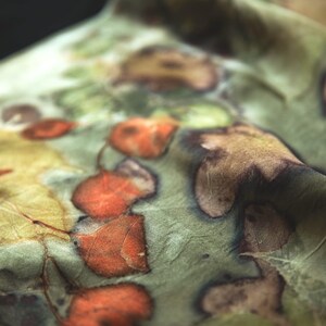 May include: A piece of fabric featuring a botanical print with a soft sage green background. The textile displays a pattern of pressed leaves in shades of burnt orange, deep brown, and muted yellow, creating a natural, organic appearance.