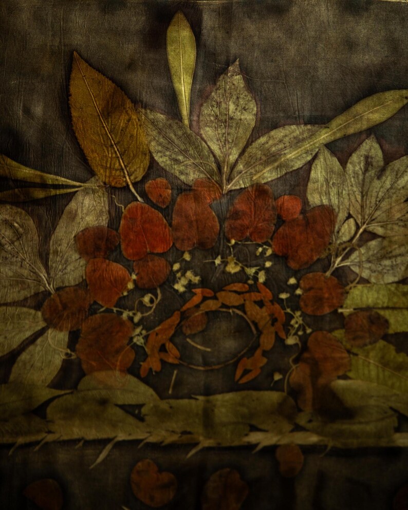 May include: A textile piece featuring a botanical print with dark brown and black background tones. The design displays an arrangement of pressed leaves in shades of olive green, golden yellow, and deep rust red, creating a layered floral pattern.