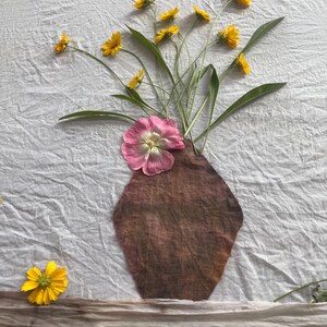 May include: A botanical arrangement on white fabric featuring a brown fabric vase shape, a large pink flower, and several small yellow flowers. The text "Botanical Arrangement Before Eco Printing" is printed at the top of the white fabric background.