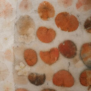 May include: A textured off-white paper surface decorated with a scattered pattern of pressed botanical elements. The design features various round and heart-shaped leaves in shades of burnt orange, rust, and muted brown, alongside small white flowers.