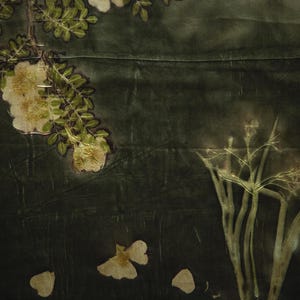 May include: A dark forest green textile featuring botanical imprints of white flowers, green leaves, and slender stems. The fabric displays a natural, organic pattern created through plant-based dyeing techniques with visible floral silhouettes.