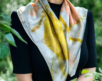 Puede incluir: Un pañuelo cuadrado de seda con estampados botánicos en tonos amarillo mostaza, melocotón suave y gris apagado. La tela muestra intrincados patrones orgánicos de hojas y tallos en toda su superficie, creando un diseño natural y multicolor.
