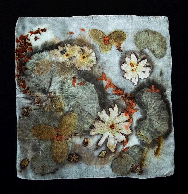 May include: A square silk scarf featuring a botanical print with pressed flowers and leaves in shades of white, muted green, and burnt orange. The fabric displays a natural, organic pattern of various plant shapes, including large rounded leaves and delicate floral blooms, set against a pale, light gray background.