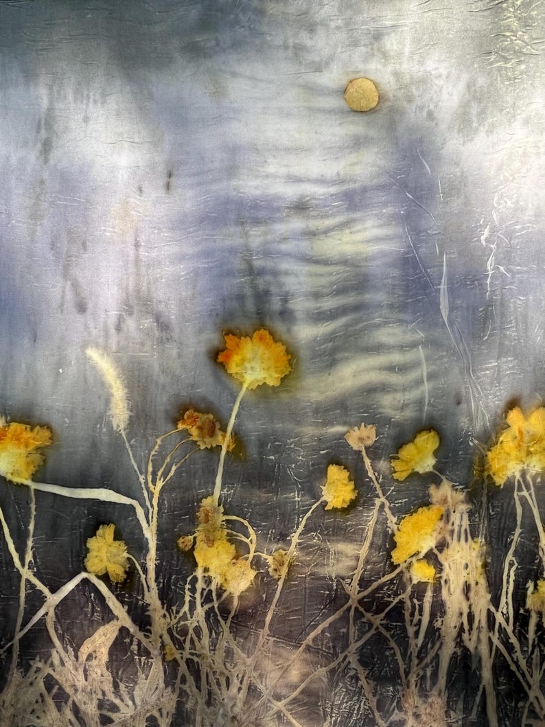 May include: A textile piece featuring a botanical print with yellow flowers and stems against a mottled, dark blue and grey background. The fabric displays a crinkled texture with a circular, light-colored shape near the top edge.