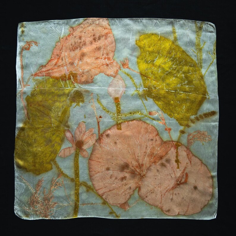 May include: A square silk scarf featuring a botanical print with large, rounded peach-colored leaves and vibrant yellow foliage against a pale, translucent grey background. The design includes delicate stems and small floral elements.