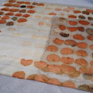 May include: A rectangular off-white textile featuring a repeating pattern of pressed orange and brown leaf prints arranged in rows. The fabric has a semi-sheer appearance with visible botanical imprints that vary in color intensity and shape.