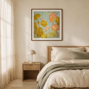 May include: A square framed wall art piece featuring a botanical illustration of lily pads and pink flowers in shades of olive green, yellow, and soft pink against a light blue background, displayed in a dark wood frame on a neutral wall.