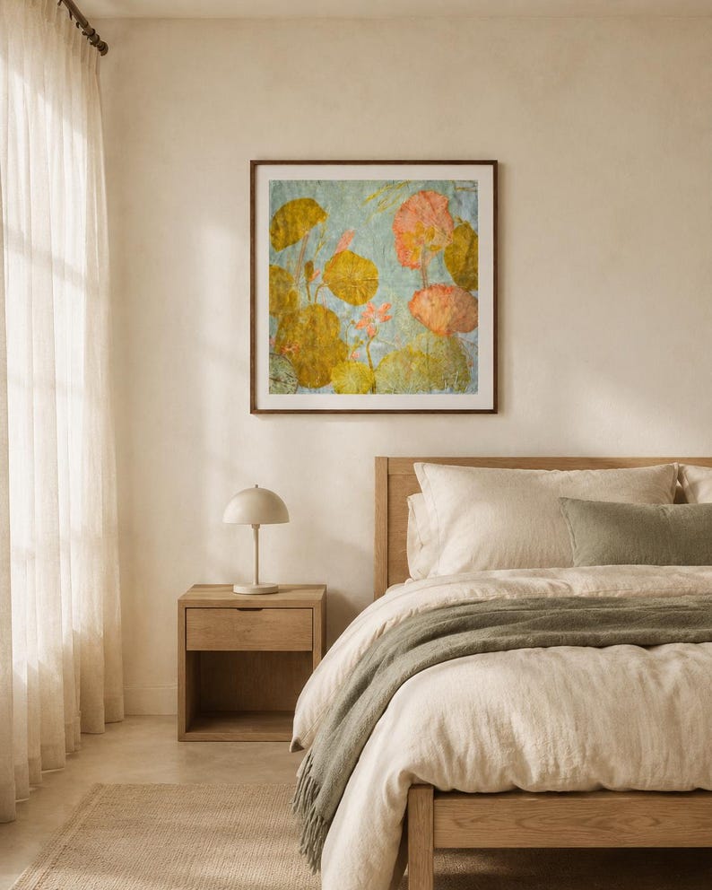 May include: A square framed wall art piece featuring a botanical illustration of lily pads and pink flowers in shades of olive green, yellow, and soft pink against a light blue background, displayed in a dark wood frame on a neutral wall.