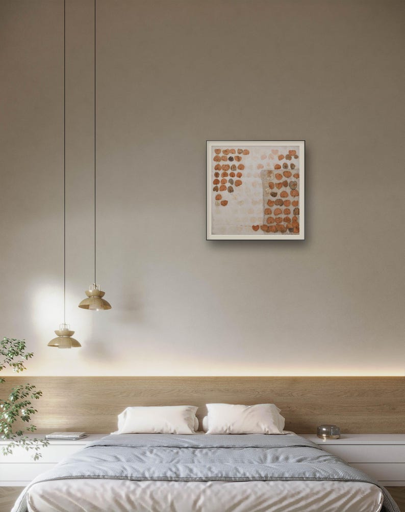 K&ouml;nnte beinhalten: Ein quadratisches gerahmtes Wandbild mit einer gitterartigen Anordnung kleiner, kreisf&ouml;rmiger, rostfarbener und brauner strukturierter Formen auf hellem, cremewei&szlig;em Hintergrund, pr&auml;sentiert in einem schlichten, d&uuml;nnen, dunklen Rahmen.