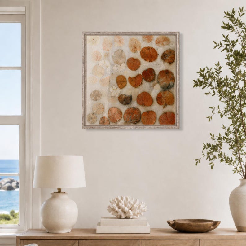 May include: A square wall art piece in a light-coloured frame featuring a grid-like arrangement of circular, textured elements in shades of burnt orange, rust, and cream. The composition displays varied organic shapes with a layered, tactile appearance.