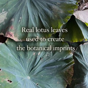 May include: A collection of large, overlapping green lotus leaves with visible veins and natural textures. The text "Real lotus leaves used to create the botanical imprints" is centered over the leaves in a clean, white, sans-serif font.