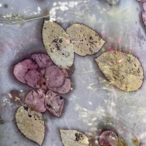 May include: Close-up of a textile with a botanical print. The fabric features a pattern of leaves in shades of pink, beige, and brown, with a light gray background. The leaves have a speckled appearance, creating a natural, organic design.