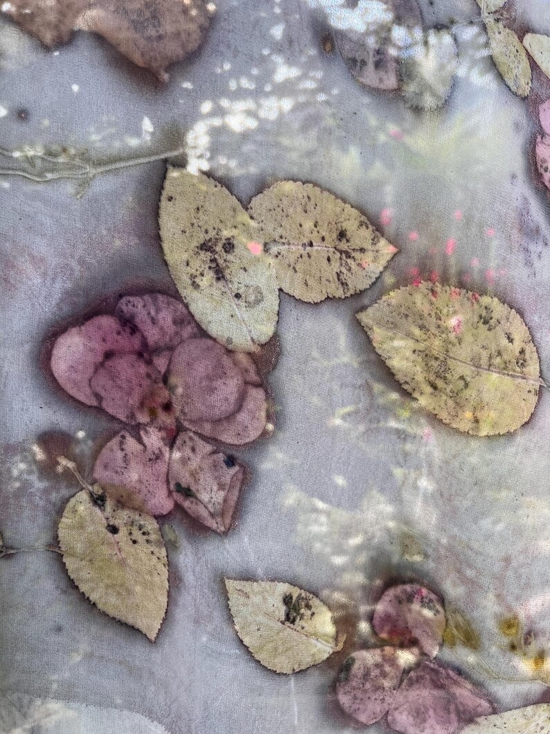 May include: Close-up of a textile with a botanical print. The fabric features a pattern of leaves in shades of pink, beige, and brown, with a light gray background. The leaves have a speckled appearance, creating a natural, organic design.