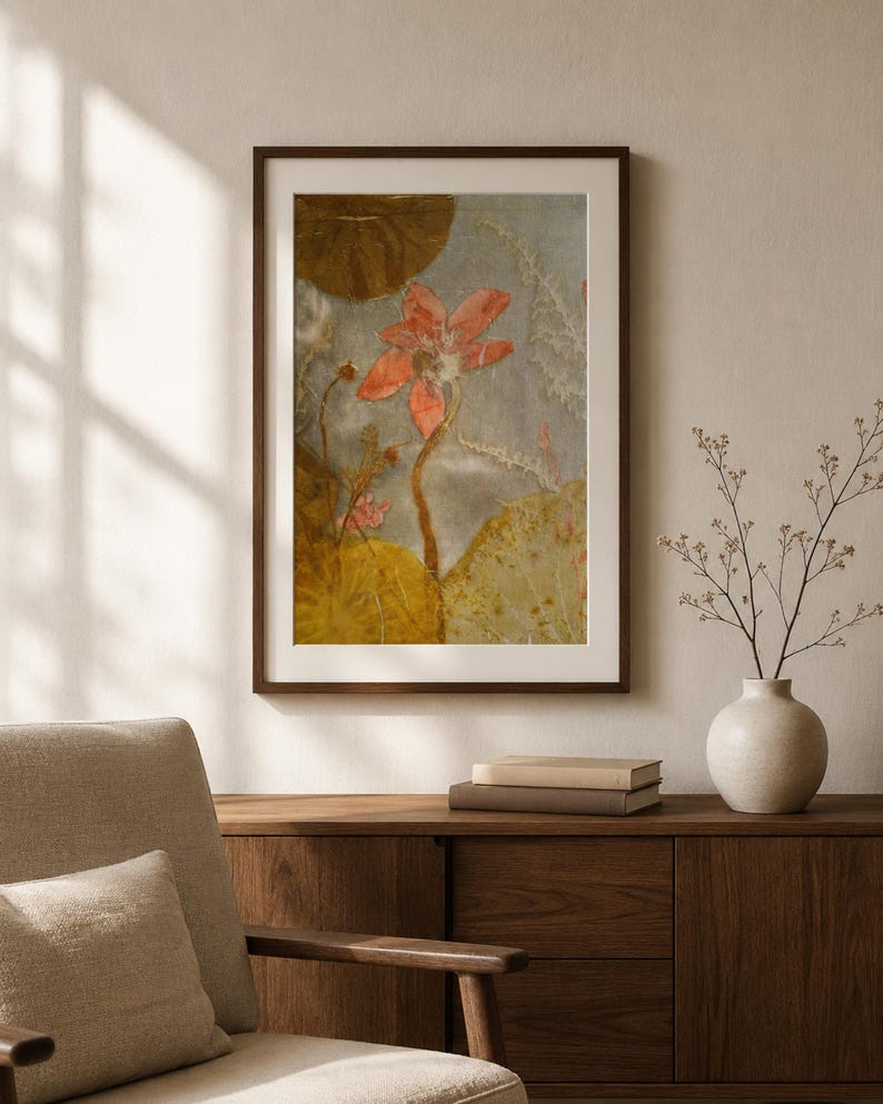 May include: A framed wall art print featuring a central coral-colored lotus flower with a long stem, surrounded by large, textured golden-brown lily pads and delicate white botanical elements against a soft, muted gray background.