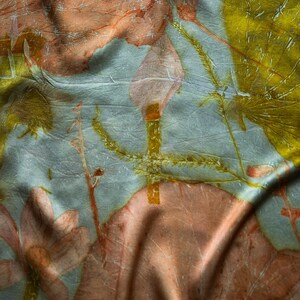 May include: A light blue fabric featuring a botanical print with large, soft pink flower shapes and vibrant yellow leaf patterns. The textile has a subtle, crinkled texture with visible folds that create depth across the surface of the material.