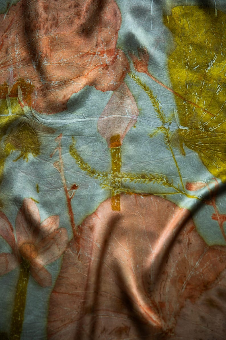 May include: A light blue fabric featuring a botanical print with large, soft pink flower shapes and vibrant yellow leaf patterns. The textile has a subtle, crinkled texture with visible folds that create depth across the surface of the material.