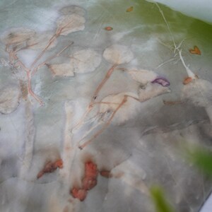 May include: A semi-sheer fabric featuring a botanical print with muted green, gray, and white tones. The surface displays organic leaf and stem patterns in soft, faded shades of orange, brown, and purple, creating a layered, natural appearance.