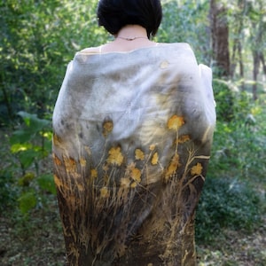 May include: A rectangular scarf featuring a botanical print with yellow flower silhouettes and dark brown foliage patterns on a gradient background that transitions from a light grey top to a deep brown bottom, draped over the shoulders.