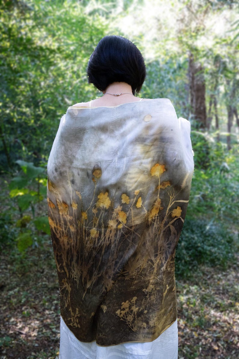 May include: A rectangular scarf featuring a botanical print with yellow flower silhouettes and dark brown foliage patterns on a gradient background that transitions from a light grey top to a deep brown bottom, draped over the shoulders.