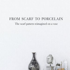May include: A black and white porcelain vase with a botanical pattern, positioned next to a stone Buddha head sculpture, a small grey vessel, and a tall white textured vase. The text reads: FROM SCARF TO PORCELAIN. The scarf pattern reimagined on a vase.