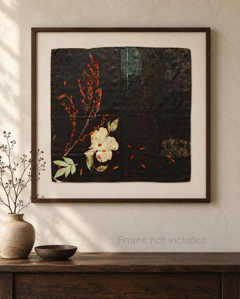 May include: A square wall art piece featuring a dark black background with a botanical print of a white flower and red foliage. The artwork is displayed within a simple dark brown frame, showcasing a clean composition with subtle textures.