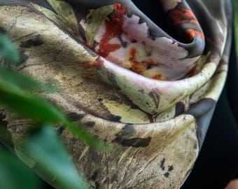 May include: A square scarf featuring a botanical print with earthy tones of brown, beige, and muted green, accented by vibrant orange and deep red leaf patterns. The fabric displays intricate, detailed textures of foliage and organic plant imprints.