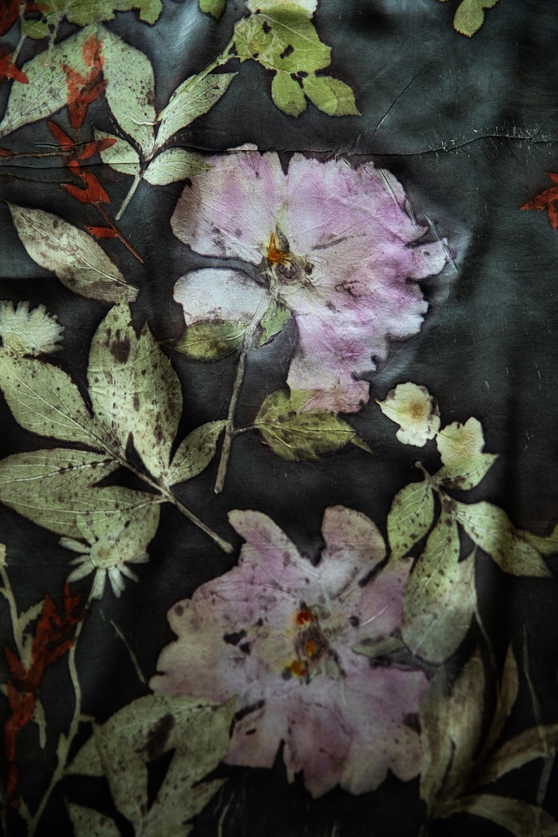 May include: Close-up of a textile with a botanical print. The design features large, pale pink flowers and green leaves with a dark background. The leaves and flowers have a textured, pressed appearance, creating a natural, artistic aesthetic.