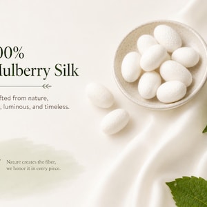 May include: A small ceramic bowl filled with white mulberry silk cocoons, accompanied by two loose cocoons and green leaves. The text reads 100% Mulberry Silk, Crafted from nature, soft, luminous, and timeless, and Nature creates the fiber, we honor it in every piece.