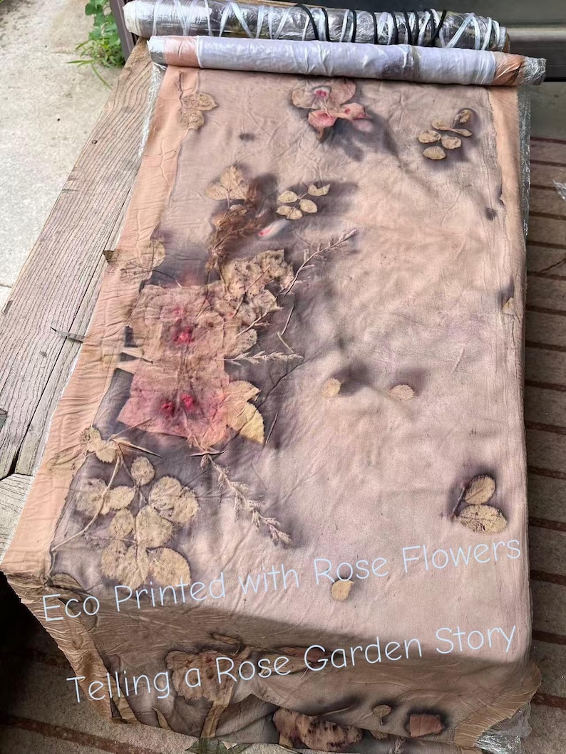 May include: A rectangular fabric runner featuring botanical eco-prints of rose flowers and leaves in shades of brown, tan, and muted pink. The text "Eco Printed with Rose Flowers Telling a Rose Garden Story" is printed in white across the lower section.