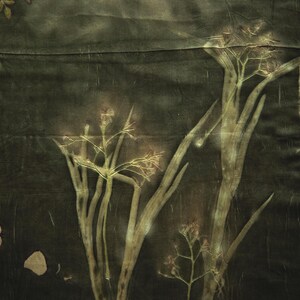 May include: A dark olive green fabric featuring botanical prints of tall flowering plants and scattered leaves. The textile displays a natural, earthy aesthetic with visible plant silhouettes in lighter shades of green and tan against a dark background.