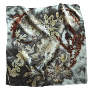 May include: A square scarf featuring a botanical print with dark gray and white marbled background tones. The fabric displays detailed imprints of various leaves and flowers in shades of deep rust, muted green, and cream throughout the surface.
