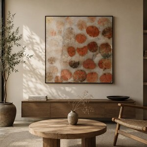 May include: A square wall art piece featuring a repeating pattern of circular, orange-toned botanical leaf prints on a light, textured background, enclosed within a thin, dark frame. The artwork displays a series of organic, rounded shapes.