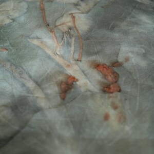May include: A piece of fabric featuring a botanical print with muted sage green and gray tones. The textile displays organic leaf and stem imprints in shades of light brown, tan, and burnt orange, creating a natural, textured, and layered appearance.