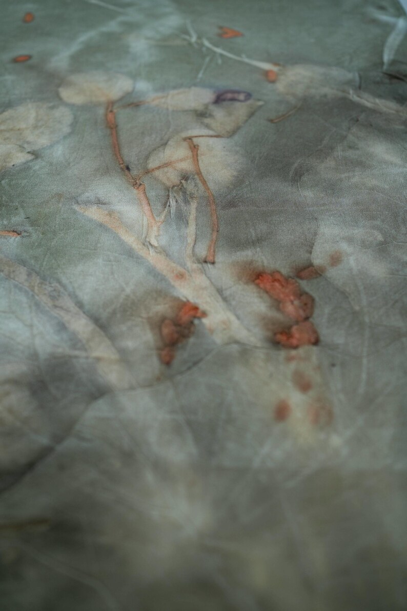 May include: A piece of fabric featuring a botanical print with muted sage green and gray tones. The textile displays organic leaf and stem imprints in shades of light brown, tan, and burnt orange, creating a natural, textured, and layered appearance.