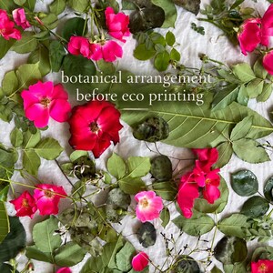 May include: A botanical arrangement of vibrant pink and red rose blossoms mixed with various green leaves and foliage, featuring the white text overlay that reads botanical arrangement before eco printing, scattered across a white fabric surface.