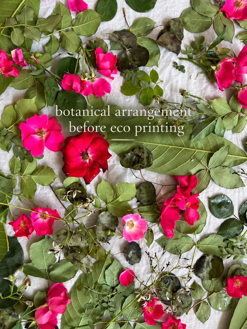May include: A botanical arrangement of vibrant pink and red rose blossoms mixed with various green leaves and foliage, featuring the white text overlay that reads botanical arrangement before eco printing, scattered across a white fabric surface.