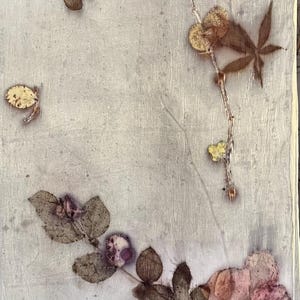 May include: A rectangular piece of off-white fabric featuring a botanical print with pressed pink flowers and dark brown leaves. The natural plant elements are arranged in a scattered pattern across the textured, light-colored textile surface.