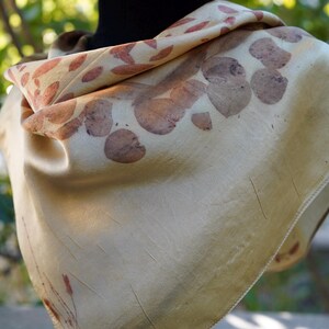 Pu&ograve; includere: Un foulard quadrato color crema chiaro caratterizzato da una stampa botanica con motivi di foglie e steli color bruno-rossastro sparsi. Il tessuto ha una finitura liscia e leggermente lucida con pieghe visibili e un orlo cucito.