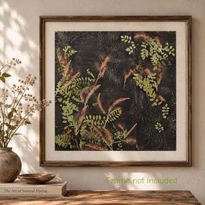 May include: A square wall art print featuring a dark, textured charcoal background with pressed green and reddish-brown fern-like foliage. The artwork is encased in a thin, dark brown wooden frame with a light-colored mat border.
