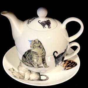 Könnte beinhalten: Weißes Keramik-Teeservice mit Katzenillustrationen. Das Set besteht aus einer Teekanne, einer Tasse und einer Untertasse. Die Katzenillustrationen sind in Grau, Schwarz und Orange gehalten. Ein charmantes Teeservice für eine Person.
