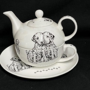 Könnte beinhalten: Ein weißes Keramik-Teeservice mit Teekanne, Tasse und Untertasse. Das Set ist mit schwarz-weißen Dalmatiner-Hunde-Illustrationen verziert. Die Untertasse hat Pfotenabdrücke. Die Teekanne hat einen Deckel mit einem kleinen weißen Knopf.