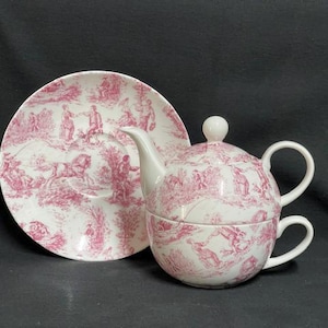Könnte beinhalten: Ein weißes Keramik-Teeservice für eine Person mit einem rosa Toile-de-Jouy-Muster. Das Set besteht aus einer Untertasse, einer Teekanne mit Deckel und einer Teetasse. Die detaillierten rosa Illustrationen zeigen verschiedene Figuren und Szenen.