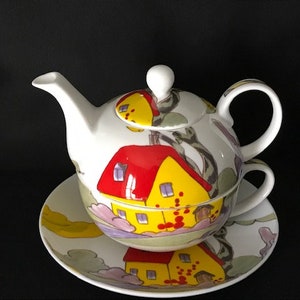 Peut inclure: Une théière en porcelaine blanche et sa soucoupe assortie avec un motif peint à la main de maisons et d'arbres. La théière a un corps rond et un bec verseur sur le côté. La soucoupe a un motif assorti et un bord festonné.