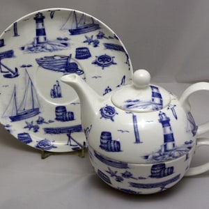 Puede incluir: Un juego de tetera y taza de té de porcelana blanca con un diseño náutico azul y blanco. El juego incluye faros, veleros, ancras y barriles.