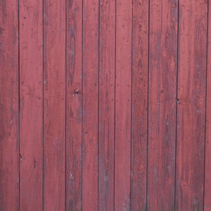 May include: A close-up of a weathered wooden wall painted a deep red color. The wood planks are vertical and have a rustic, aged appearance.