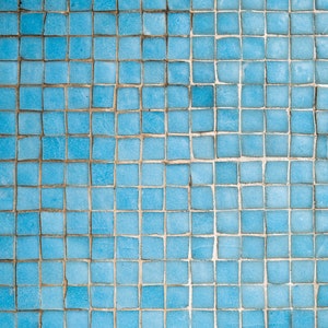May include: A close-up of a wall covered in small, square, blue tiles. The tiles are arranged in a grid pattern and have a slightly worn appearance.
